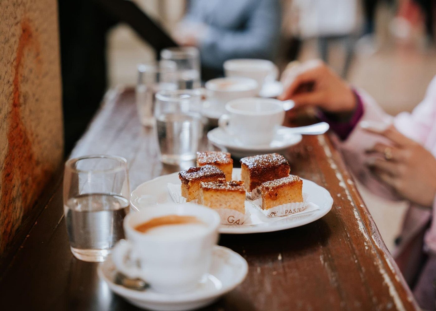 Start your Bologna food tour with a warm macchiato and a sweet treat! A creamy macchiato served in a white cup next to a slice of cake on a café table in Bologna
