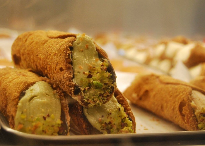 I Dolci di Nonna Vincenza – Sicilian Cannoli Heaven Pistachio cannoli with crisp golden shells, filled with ricotta cream and topped with crushed pistachios, displayed at a Sicilian pastry shop