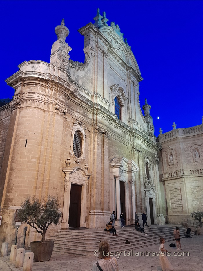 A view of the Cattedrale Maria Santissima della Madia in Monopoli glowing warmly at dusk, with the Baroque façade illuminated against the evening sky