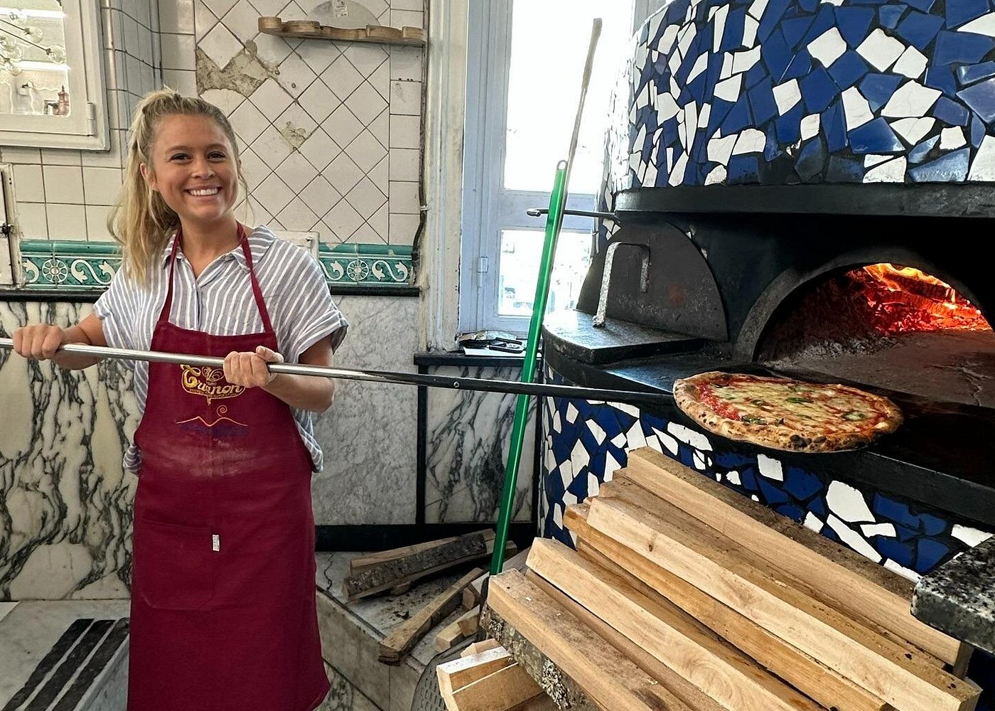 Guest pulling a freshly baked pizza from a traditional wood-fired oven during a Naples pizza-making class