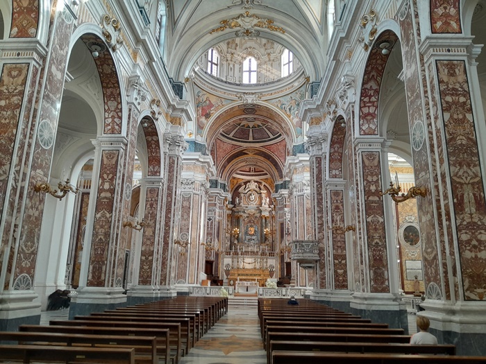 The interior of Monopoli Cathedral with ornate arches, marble columns, and soft golden light