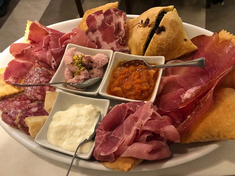 Traditional Emilia-Romagna cold cut platter with assorted dips and cheese Platter of Emilia-Romagna cold cuts including culatello, coppa, ham, and mortadella, served with small bowls of dips and soft cheese